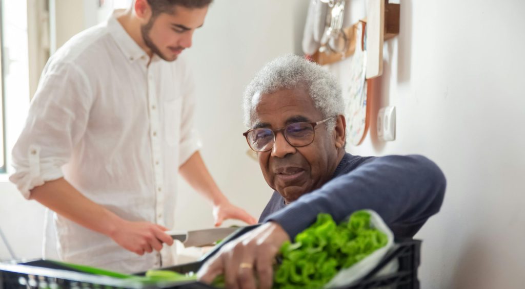 A senior man supported by a volunteer with groceries at home.